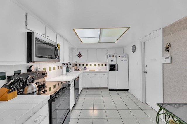 kitchen featuring black appliances, light tile patterned flooring, white cabinetry, and decorative backsplash