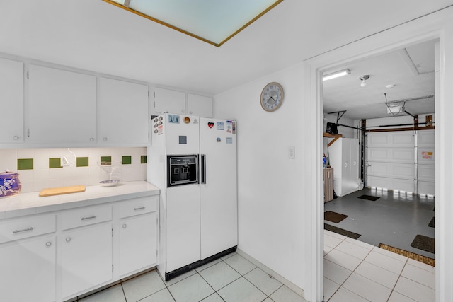 kitchen with light tile patterned floors, white refrigerator with ice dispenser, backsplash, and white cabinets