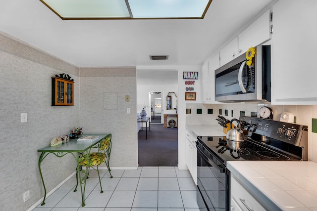 kitchen featuring tasteful backsplash, white cabinets, light tile patterned floors, tile countertops, and black electric range