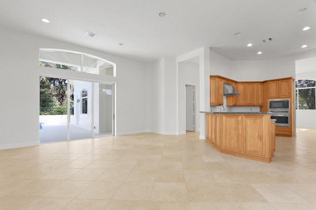 kitchen featuring appliances with stainless steel finishes, light tile patterned floors, a towering ceiling, and wall chimney range hood