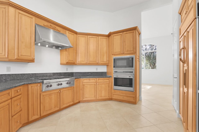 kitchen featuring dark stone countertops, light tile patterned flooring, appliances with stainless steel finishes, and wall chimney range hood