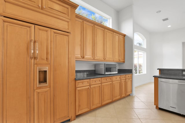 kitchen with stainless steel appliances, dark stone countertops, light tile patterned floors, and a healthy amount of sunlight