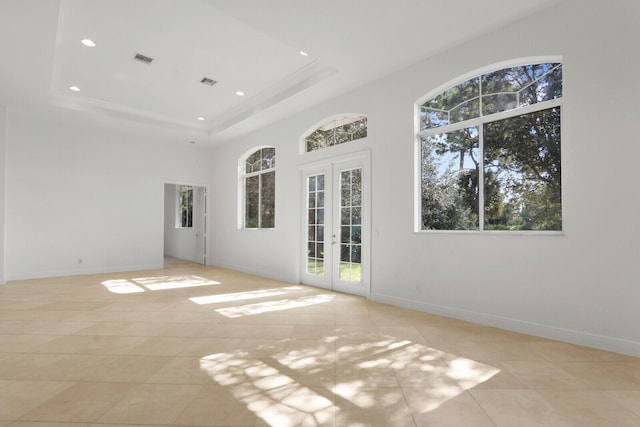 tiled empty room featuring french doors and a raised ceiling