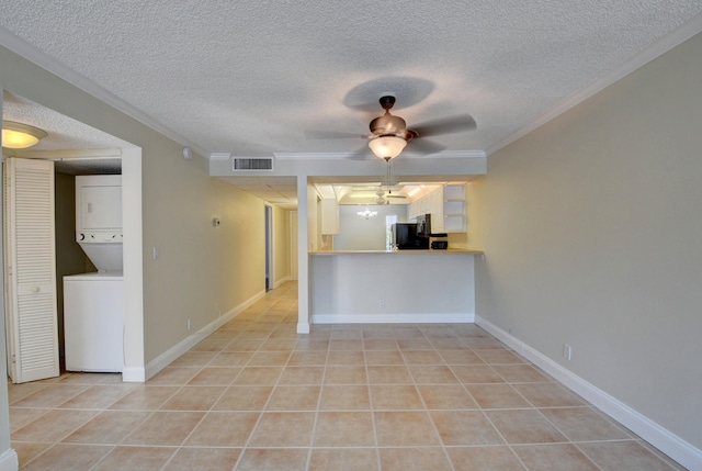 spare room featuring stacked washer / dryer, crown molding, a textured ceiling, and ceiling fan