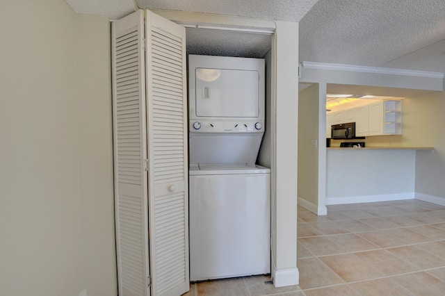 laundry room with a textured ceiling, stacked washer / dryer, light tile patterned floors, and crown molding