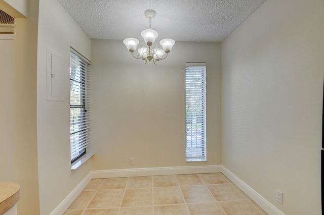 empty room with a textured ceiling, an inviting chandelier, and light tile patterned floors