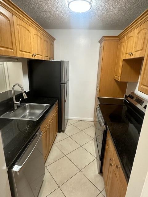 kitchen with a textured ceiling, appliances with stainless steel finishes, light tile patterned flooring, and sink