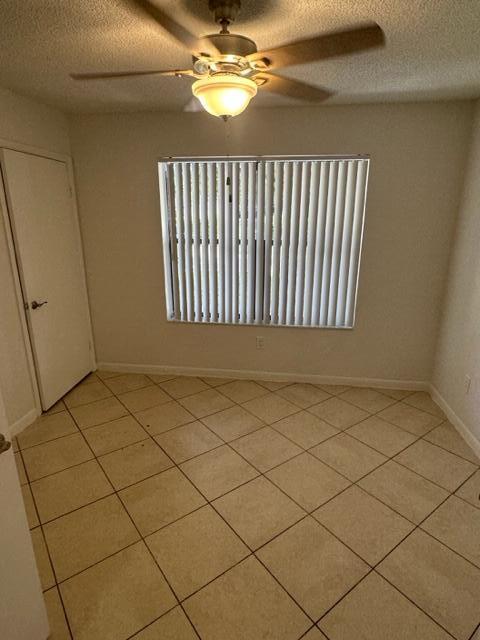 empty room featuring a textured ceiling, light tile patterned floors, and ceiling fan