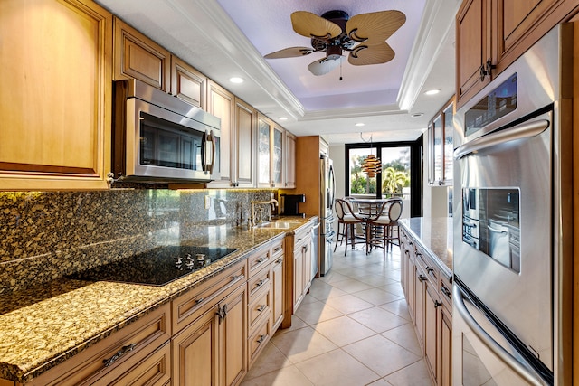 kitchen featuring light tile patterned floors, appliances with stainless steel finishes, ceiling fan, a tray ceiling, and light stone counters