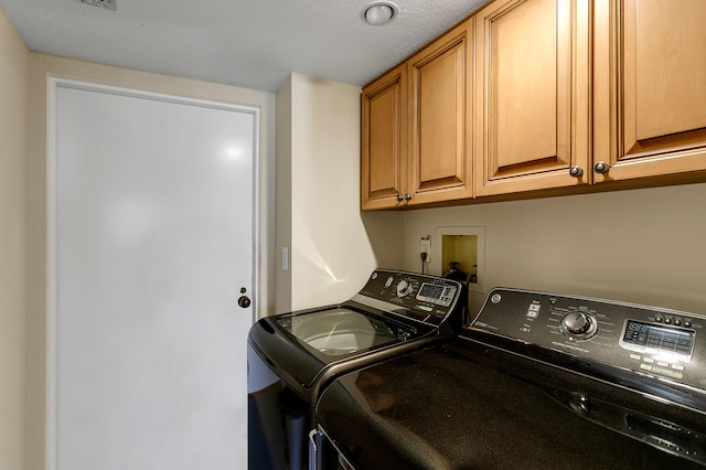 laundry room featuring independent washer and dryer, a textured ceiling, and cabinets