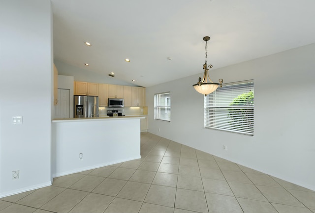 kitchen featuring light brown cabinetry, stainless steel appliances, vaulted ceiling, and a healthy amount of sunlight