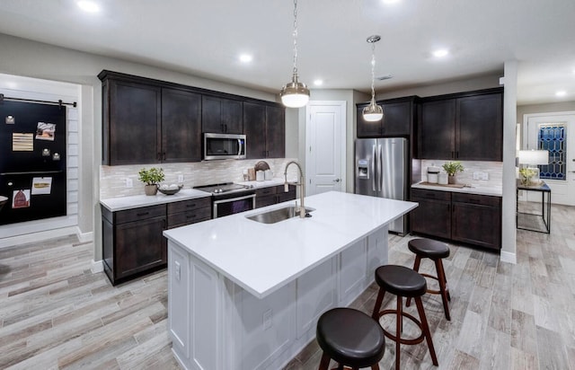 kitchen with pendant lighting, sink, a center island with sink, stainless steel appliances, and light hardwood / wood-style floors