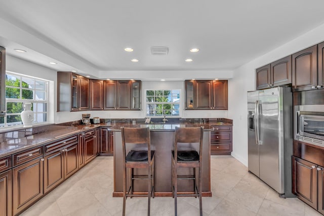 kitchen featuring stainless steel refrigerator with ice dispenser, a kitchen island, a healthy amount of sunlight, and a breakfast bar area