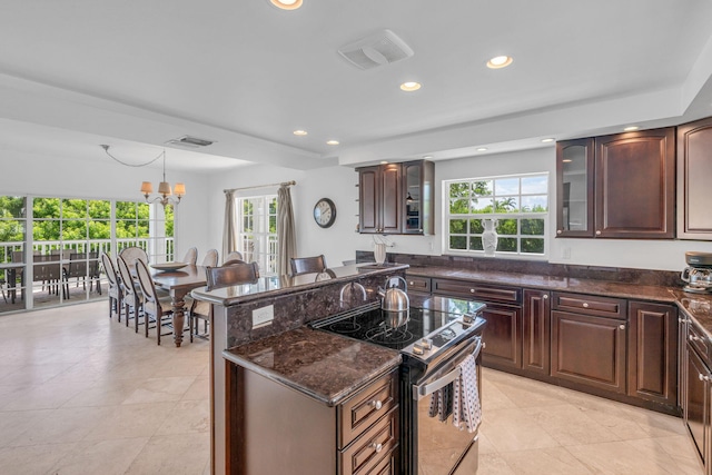 kitchen with pendant lighting, dark brown cabinets, electric range, dark stone countertops, and an inviting chandelier