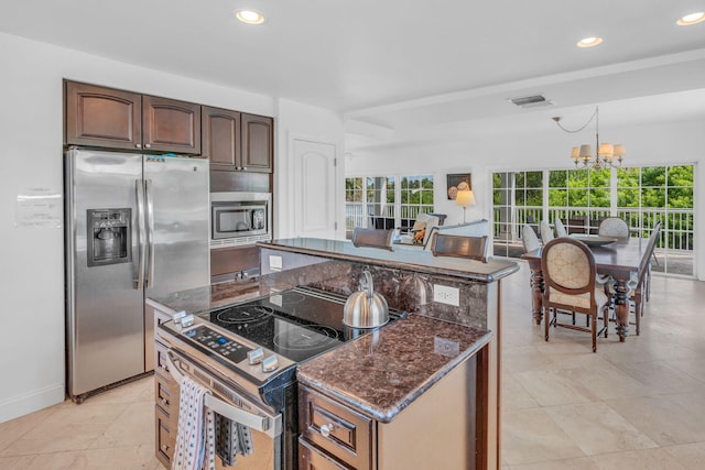 kitchen featuring dark stone counters, a kitchen island, an inviting chandelier, stainless steel appliances, and dark brown cabinetry