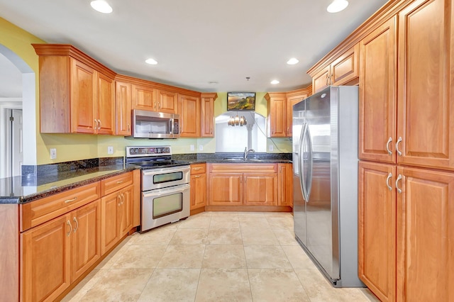 kitchen featuring dark stone countertops, sink, light tile patterned floors, and stainless steel appliances