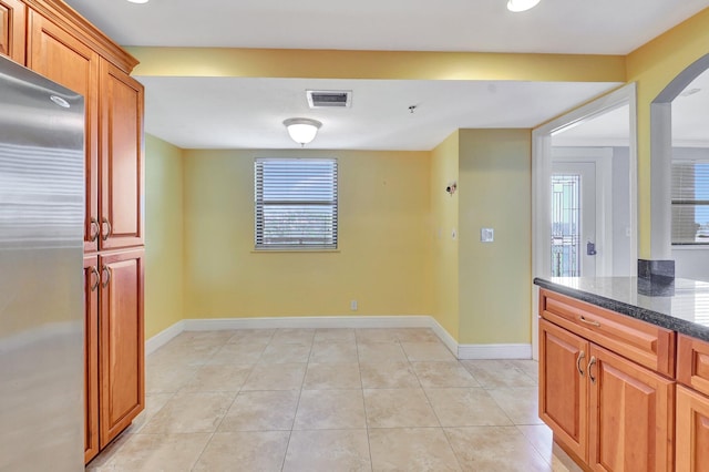 kitchen featuring light tile patterned flooring, stainless steel fridge, dark stone counters, and a healthy amount of sunlight