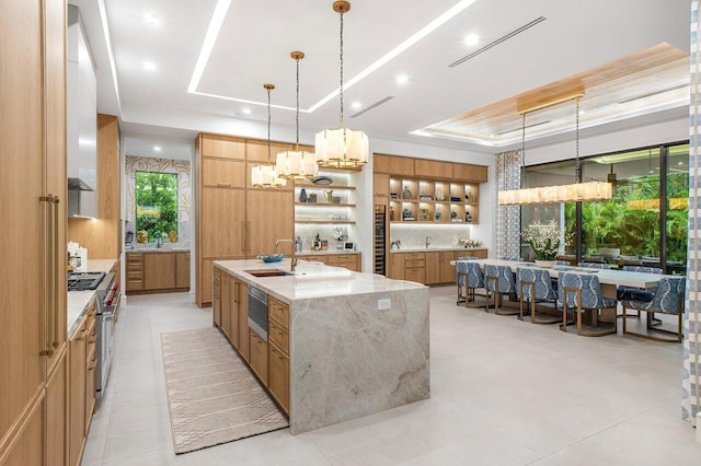 kitchen with pendant lighting, a large island with sink, white cabinetry, range with two ovens, and light stone countertops