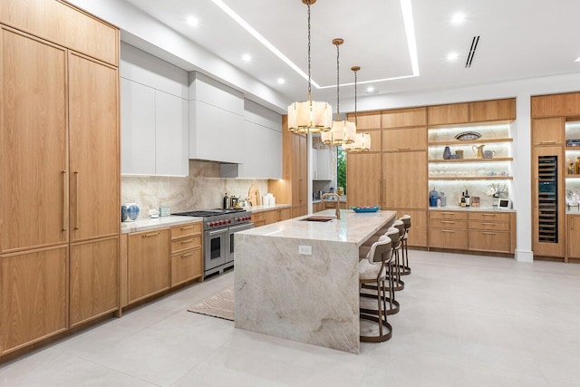 kitchen featuring white cabinetry, backsplash, light stone countertops, decorative light fixtures, and a kitchen island with sink