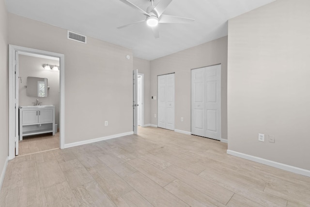 unfurnished bedroom featuring multiple closets, ceiling fan, sink, light hardwood / wood-style flooring, and ensuite bathroom