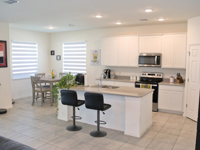 kitchen with appliances with stainless steel finishes, a kitchen island with sink, sink, and white cabinetry