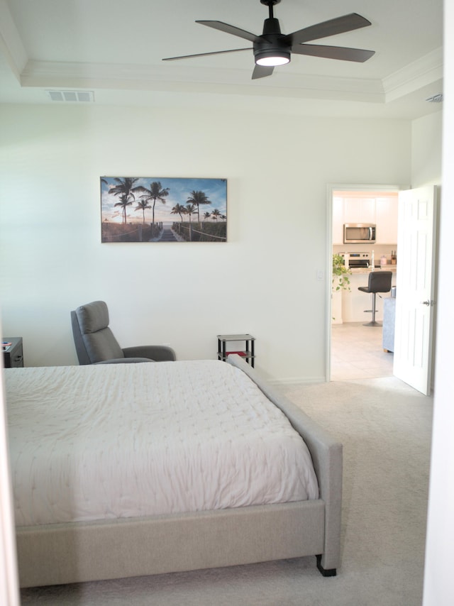 bedroom with a tray ceiling, ornamental molding, ceiling fan, and light colored carpet