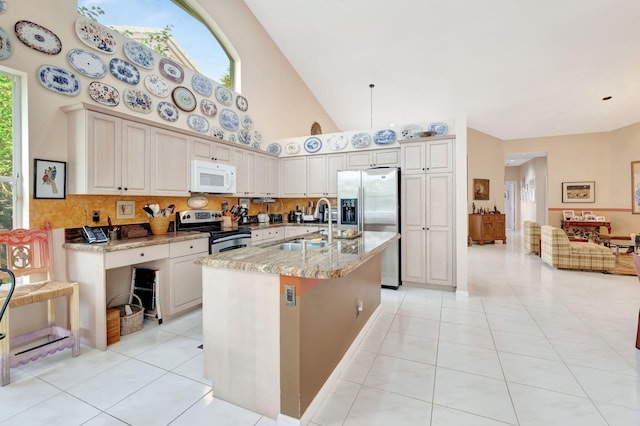 kitchen featuring light tile patterned floors, a center island with sink, high vaulted ceiling, stainless steel appliances, and light stone countertops