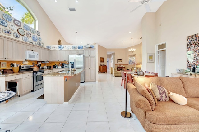 kitchen featuring cream cabinetry, hanging light fixtures, ceiling fan with notable chandelier, stainless steel appliances, and a high ceiling