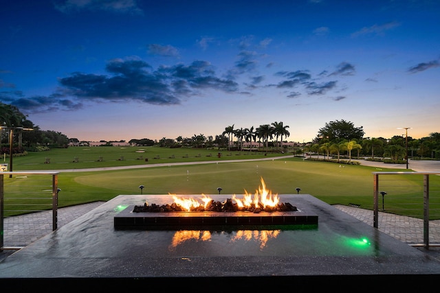 pool at dusk featuring an outdoor fire pit and a yard