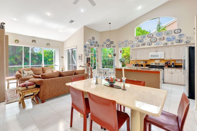 tiled dining space with high vaulted ceiling, ceiling fan, plenty of natural light, and sink