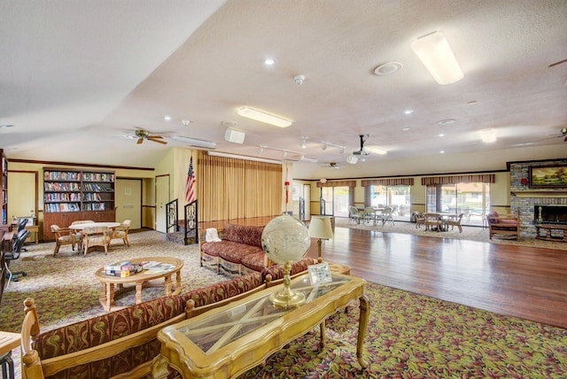 living room featuring a textured ceiling, wood-type flooring, lofted ceiling, a large fireplace, and ceiling fan