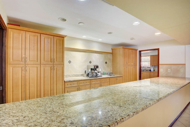 kitchen featuring light stone counters, light brown cabinets, sink, kitchen peninsula, and decorative backsplash