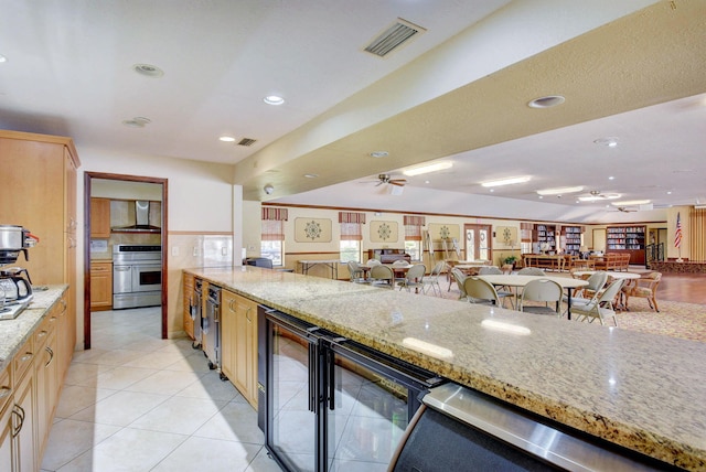 kitchen featuring light stone counters, wall chimney exhaust hood, light brown cabinets, light tile patterned floors, and stainless steel range