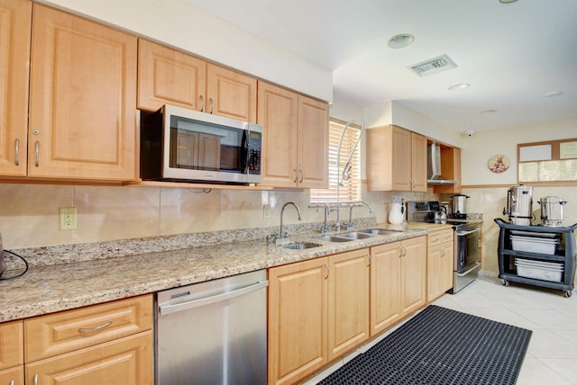 kitchen with light stone counters, wall chimney range hood, appliances with stainless steel finishes, light tile patterned floors, and light brown cabinetry