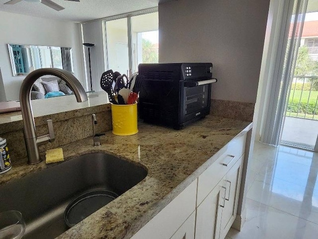 kitchen featuring white cabinets, light tile patterned flooring, light stone counters, and sink