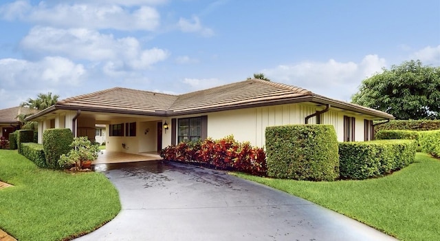 view of front facade featuring an attached carport, driveway, a front lawn, and a tile roof