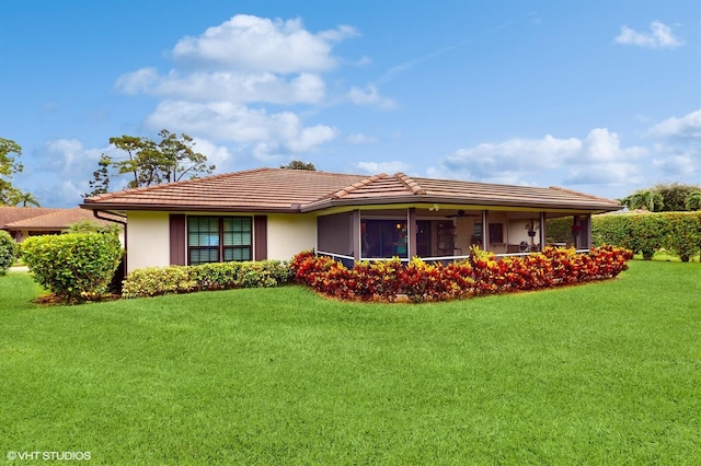ranch-style house featuring a front yard, a tiled roof, a sunroom, and stucco siding