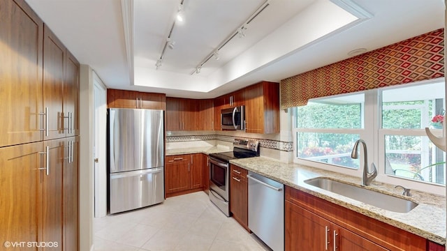 kitchen with appliances with stainless steel finishes, a sink, rail lighting, and light stone counters