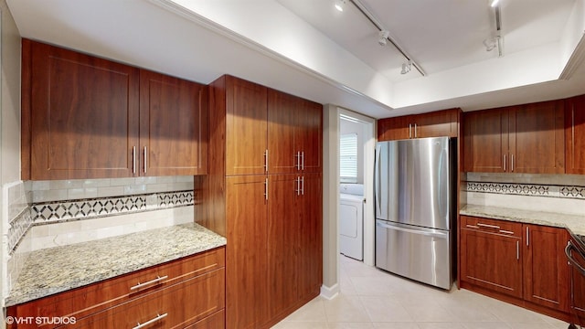 kitchen featuring tasteful backsplash, track lighting, light tile patterned floors, freestanding refrigerator, and light stone countertops