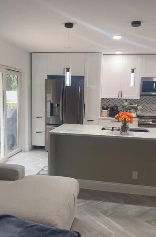 kitchen featuring decorative backsplash, hanging light fixtures, white cabinets, appliances with stainless steel finishes, and lofted ceiling