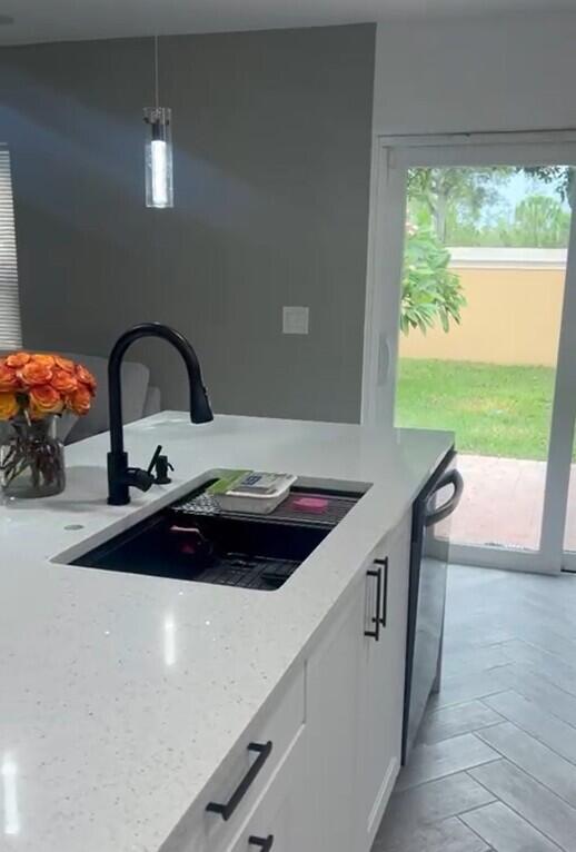 kitchen featuring light stone counters, stainless steel dishwasher, white cabinets, sink, and decorative light fixtures