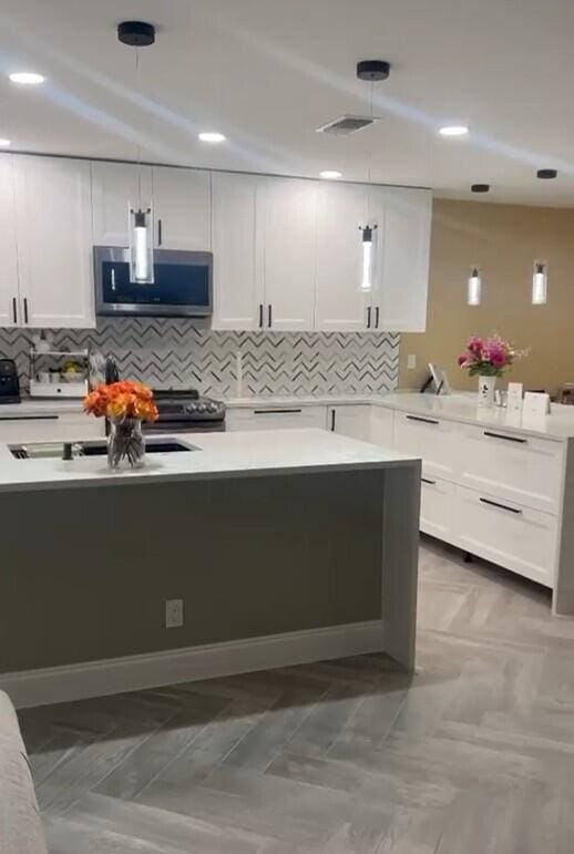 kitchen with tasteful backsplash, hanging light fixtures, and white cabinets