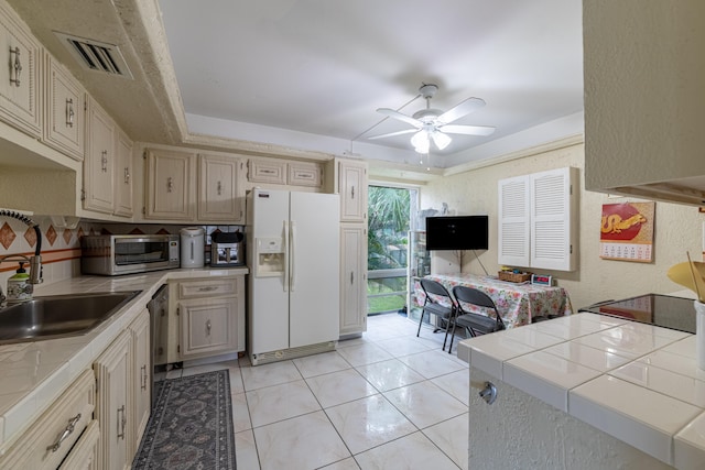 kitchen featuring light tile patterned flooring, ceiling fan, tile counters, white fridge with ice dispenser, and sink