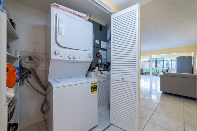 laundry area featuring a textured ceiling, heating unit, light tile patterned floors, and stacked washing maching and dryer