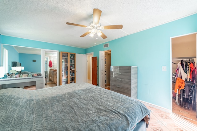 bedroom featuring ceiling fan, a textured ceiling, a walk in closet, a closet, and ensuite bath