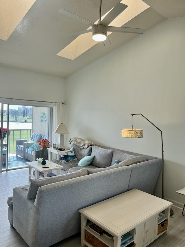 living room featuring hardwood / wood-style flooring, ceiling fan, and lofted ceiling with skylight