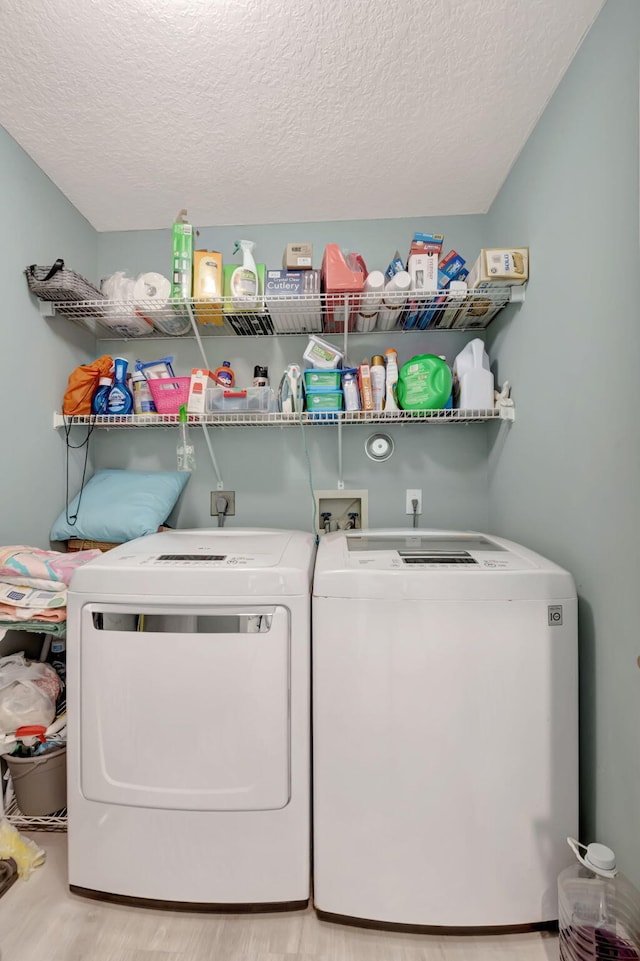 clothes washing area with washing machine and dryer, a textured ceiling, and light wood-type flooring