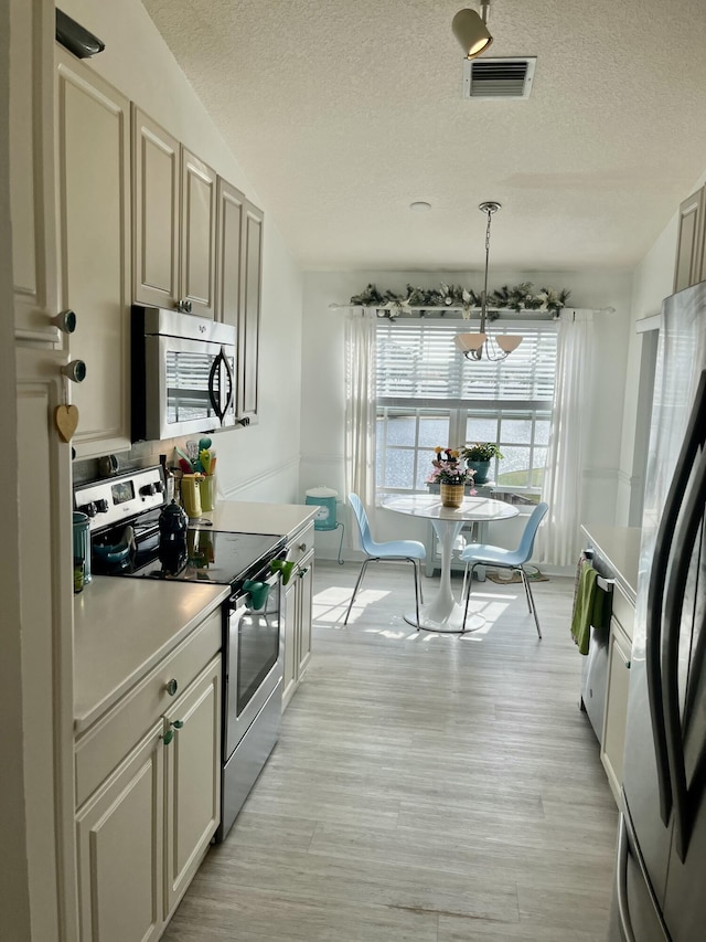 kitchen with stainless steel appliances, an inviting chandelier, pendant lighting, a textured ceiling, and light hardwood / wood-style floors