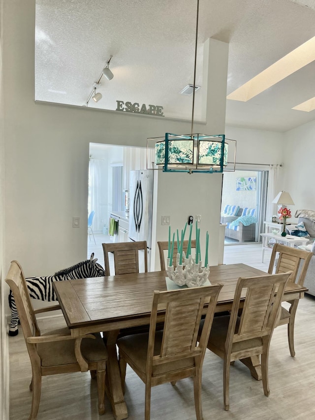 dining space with a textured ceiling, light hardwood / wood-style floors, and rail lighting