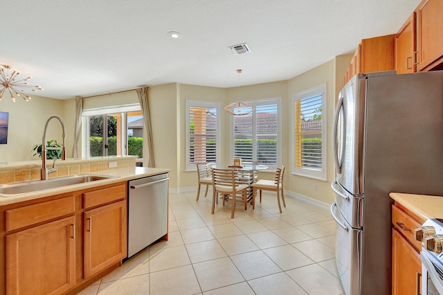 kitchen with light tile patterned floors, pendant lighting, stainless steel appliances, an inviting chandelier, and sink